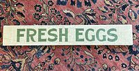 Front view of the rectangular wooden sign showing hand painted 'FRESH EGGS' text in green on white background.