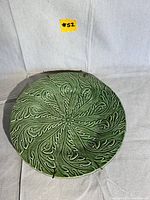 Image of the green Majolica plate with embossed leaf pattern on a cloth background.
