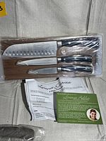 Lorena Bella black handle 4-piece knife set with Santoku knife, paring knife, and two other knives, displayed on a tray with informational papers.