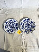 Pair of antique round porcelain plates with blue onion and floral flow blue pattern on white fabric background