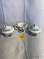 Three-piece Villeroy & Boch Citta and Campagna china set with two lidded sugar bowls and one creamer pitcher photographed on a neutral gray textile background.
