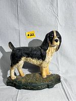 Side view of the vintage cast iron dog doorstop, showing black and white paint with tan accents and detailed fur texture.