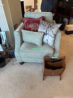 Arm chair from front, showing three cushions and vintage wooden magazine rack in front.