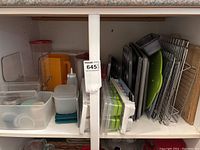 Shelf with plastic containers, juice jug, ice cube trays, and stacked baking trays and racks.