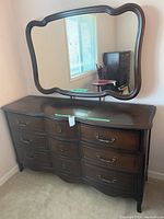 Photo of wooden dresser with mirror reflecting window and chair.