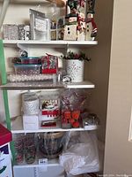 Shelves with ceramic snowman figurines, containers filled with clear glass and silver ornaments, red berry floral arrangement, and boxes of holiday decorations.