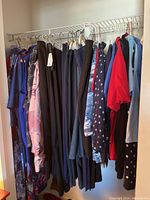 Closet rack with multiple women's garments hung, featuring dark colored trousers, house coats, and tops in various colors including blue, red, and patterned options