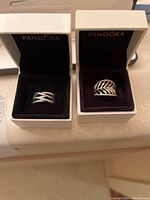 Two Pandora ring boxes each holding a sterling silver ring, one multi-row pavé and one leaf motif