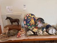 Full view of horse figurine in case, decorative plates, candle holders, and other small decor items on wooden surface