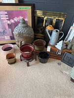 Wide view of all items grouped in front of fireplace including Buddha head, pots, picture, watering can, tree sculpture, and candles.