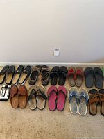 Wide view of 10 pairs of women's summer footwear arranged on carpeted floor against wall.