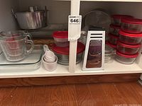 Overall view of glass bakeware and kitchen items including glass measuring cups, red-lidded glass containers, metal grater, and small measuring spoons.