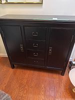 Front view of narrow black cabinet with two doors and four drawers.