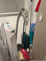 Photo of Kenmore vacuum cleaner with hose, metal extensions, an electric tower fan, ironing board, and iron visible.