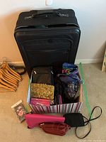 Black fabric luggage pieces stacked and box of various purses in front