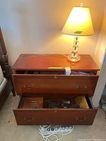 Wooden two-drawer office filing cabinet partially open showing contents.