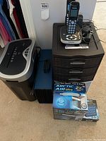 View of Omnitech shredder, Panasonic cordless phones on plastic drawer unit, Artic Air Ultra fan box and filter box, blue file box