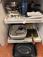 Lower cabinet shelf with electric frypan, small pans, roasting pan, and other items.