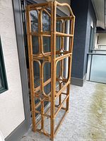 Full side view of the tall rattan shelving unit showing its height, rattan frame structure, and how the shelves are positioned inside.