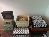 Full view showing seven storage items including green boxes, woven basket, damask pattern box, and black pattern box
