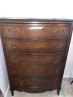 Front view of the tall wood dresser showing five drawers with metal handles and a dark wood finish.