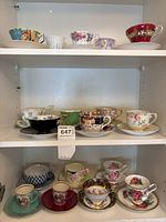 Photo showing an upper shelf with 6 teacups and saucers with floral and decorative patterns in various colors
