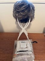 Front view of short synthetic wig on white wig stand with sealed hair care product pack in front