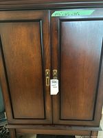 Front view showing two paneled doors of the dark wooden stereo cabinet with handles and measurement tape above indicating dimensions.