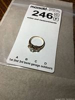 Gold ring with three stones on a white background and clear plastic bag showing lot number tag.