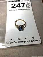 10K gold ring with light blue solitaire stone against auction note card