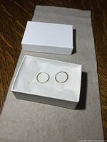 Pair of small 14K gold hoop earrings inside a white box on gray fabric background.