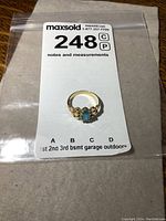 Top view of the gold ring in its plastic bag with MaxSold tag.