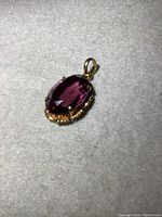 Front view of oval faceted amethyst-colored pendant on grey cloth