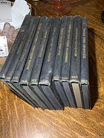 Set of 10 black hardcover repair manuals with gilt spines arranged standing side-by-side on a wooden table showing title text for identification.