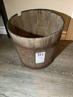 Old wooden bucket standing on a wooden floor, showing the top and inside view with visible aging and cracks on the rim.