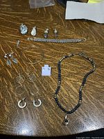 Full view of all jewelry pieces on a wooden surface including earrings, necklace, bracelet, bangle, and stone pendants