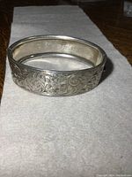 Closed view of silver bracelet showing detailed floral engraving and monogram inside.