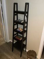 Front and side view of tapered dark modern bookshelf with five open shelves and ladder side support.