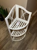 Front angled view showing the three slatted shelves, curved sides, and decorative crossbars, white paint with light wear visible on edges.