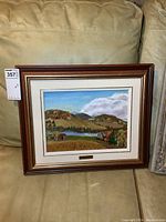 Framed oil painting depicting a rural landscape with hills, pond, and houses in autumn colors.