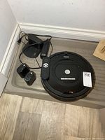 iRobot Roomba vacuum with charging dock, remote control, and other accessories placed in corner on wooden floor