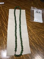 Full view of the jade bead necklace laid flat on a fabric background, showing overall length and bead arrangement.