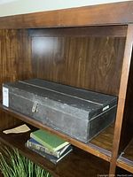 Side view of the old rectangular wooden storage box painted black, showing surface wear and brass hasp latch.