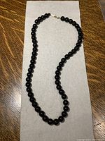 Full view of black onyx bead necklace laid flat on a light gray cloth against a wood surface background.