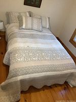 Full bed view showing quilted bedspread laid on queen bed with 2 matching pillows and 1 decorative pillow at the head.