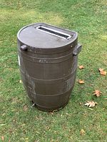 Full view of the resin rain barrel standing upright on grass, showing wood-like texture and exterior taps.