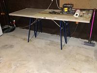 Full view of two blue metal folding sawhorses with a vintage wooden door placed on top serving as a table.