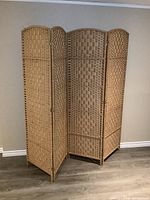 Overall view of the four-panel folding room divider screen standing upright, showing arched tops and woven rectangular pattern on natural wood tones.
