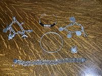 Top down photo showing all items in the lot on wood surface including two charm bracelets, one chain-link bracelet, and two bangles.