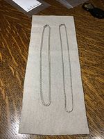 Two silver chains laid out flat on beige fabric on a wooden surface, showing full length.